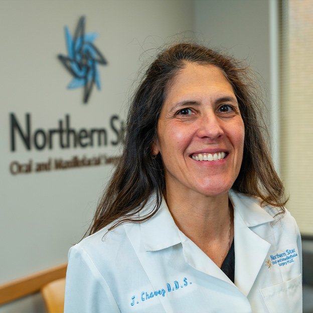 The image shows a woman standing in front of a sign with the text  NORTHERN STATE DENTAL AND MEDICAL SCHOOL  smiling at the camera, wearing a white lab coat, and posing for a portrait.