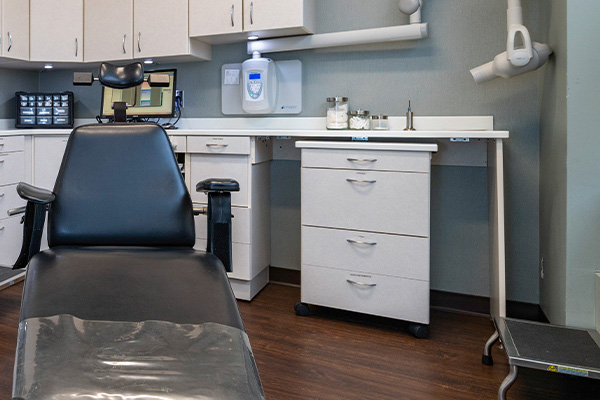 The image shows an interior view of a dental office with a modern setup, featuring a dentist s chair, examination table, and other equipment typically found in such a setting.